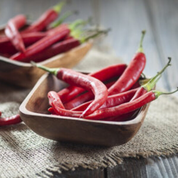 Wooden bowl of red chili peppers on jute and wood